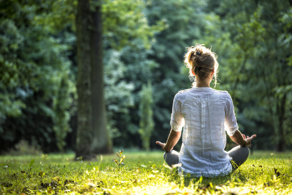 Une femme assise de dos dans l'herbe en train de méditer. 